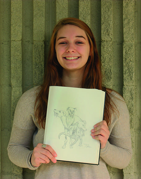 Cerebus Alive: Senior Jade Rider holds her drawing of Cerberus, the three-headed dog featured in many Greek mythological tales. Rider used her artistic ability to manifest her interests and inspirations into this visual piece. “[Jade Rider] has the ability to switch styles of drawing without losing quality,” senior Magdalena Maziarz said.