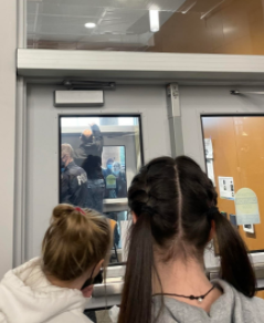 Communication Breakdown: Students watch police and students from behind the front office doors on Dec. 10. Students had confusion about lunchtime and being let back into the building on Friday. Id say it started out very positive, but then it went downhill, junior Elliot Page said.