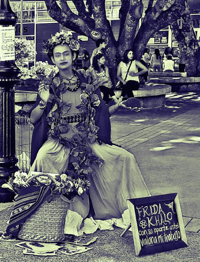 Photograph of a street performer dressed as Frida Khalo showcasing her artwork.