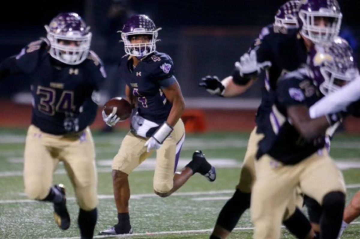 Striving for greatness: Junior Cassidy Bolong-Banks runs the ball downfield during an LSHS playoff game while senior Esteban Sedano (34) blocks for him.