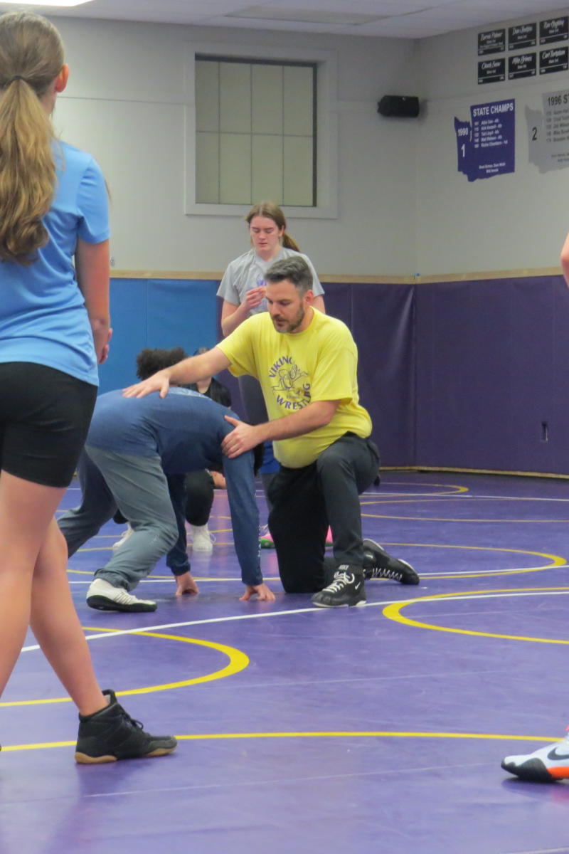 Wrestling head coach Derek Lopez demonstrates a move with assistant coach Raphil Hasegawa during the first day of girls wrestling practice .