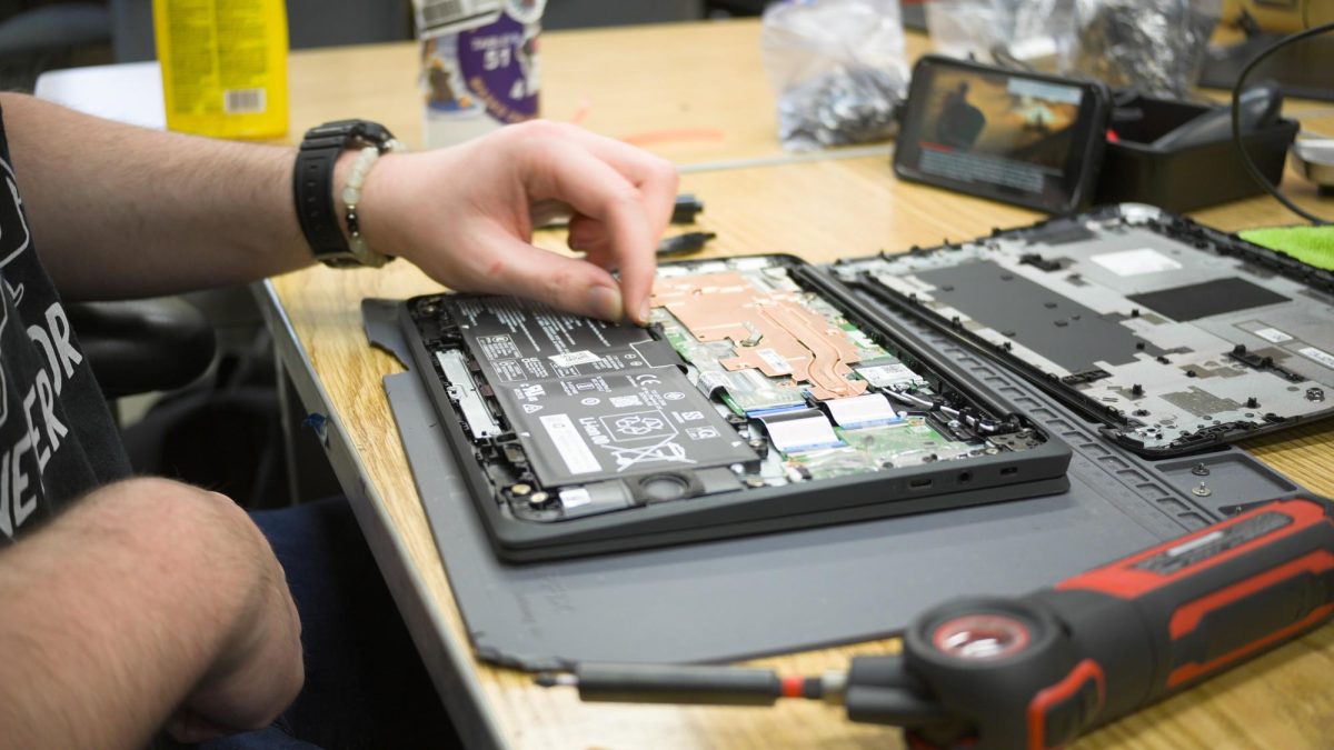 Student Technician Dane Satterlee repairs an HP G10 Chromebook, examining the internal components.